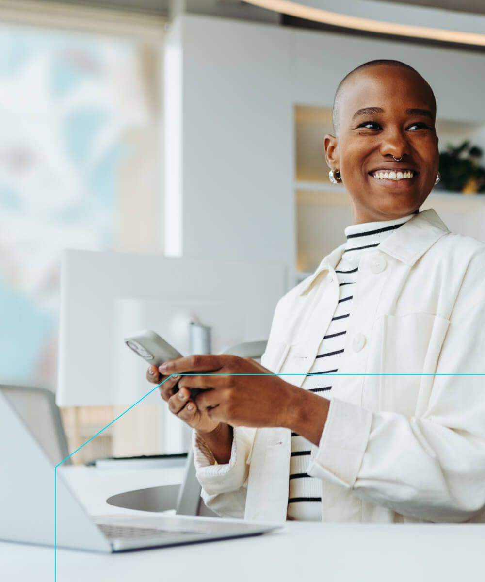 Smiling woman using phone and laptop in a bright office space - Neutrinos