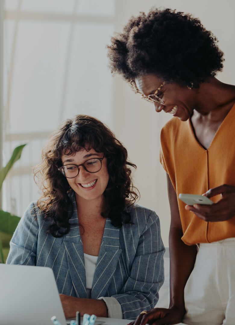 Two women smiling while working on a laptop together in a modern office - Neutrinos